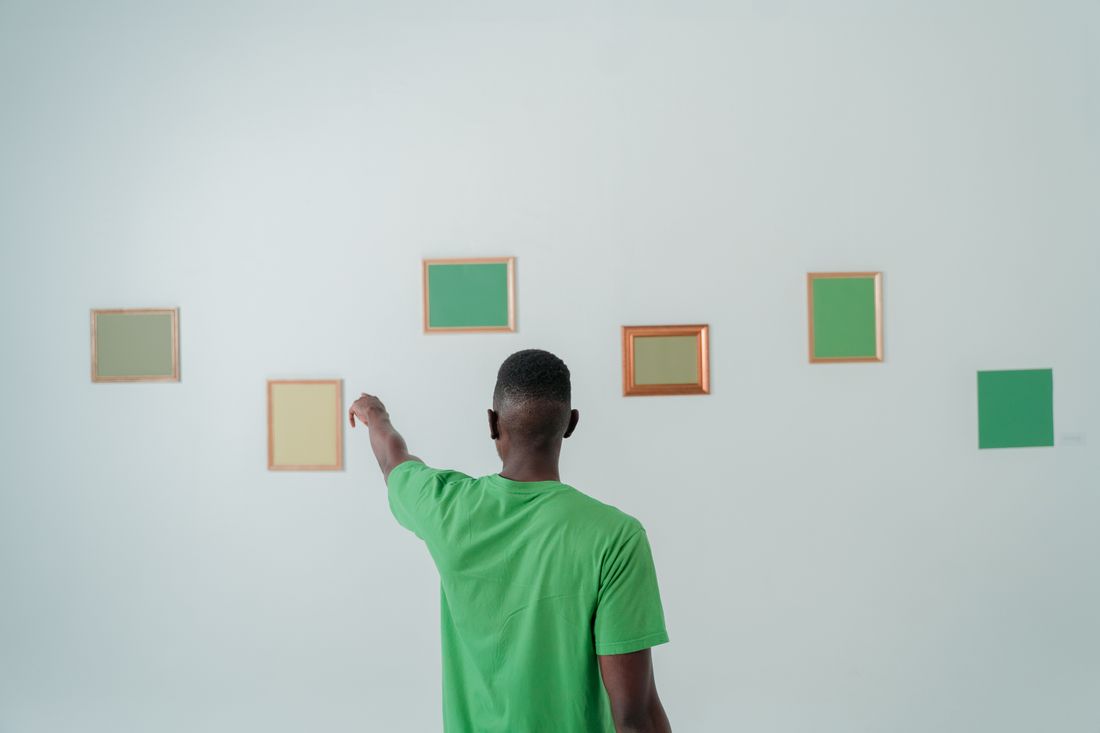 A person seen from behind pointing at a row of small framed color panels arranged on a plain white wall.