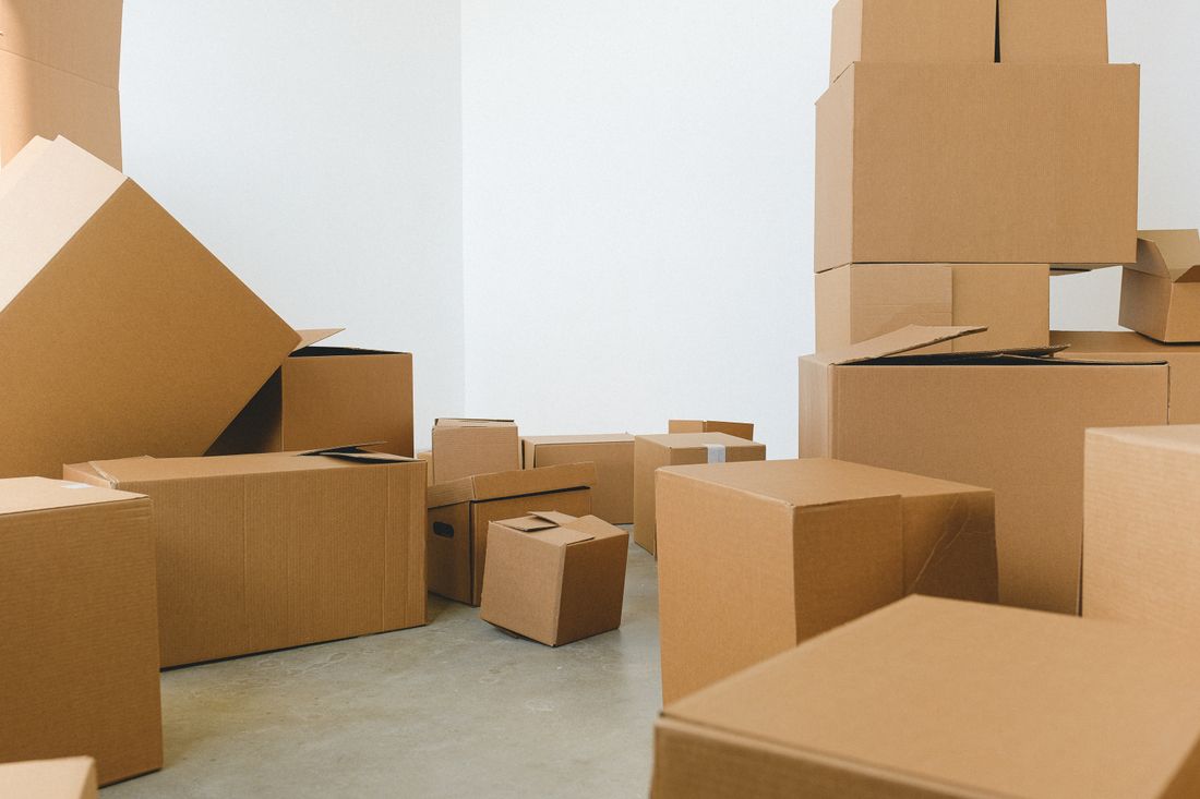 A pile of cardboard moving boxes scattered across the floor of an empty room with plain white walls