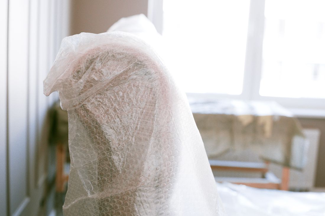 A piece of furniture wrapped in bubble wrap for protection in a bright, sunlit room before a move