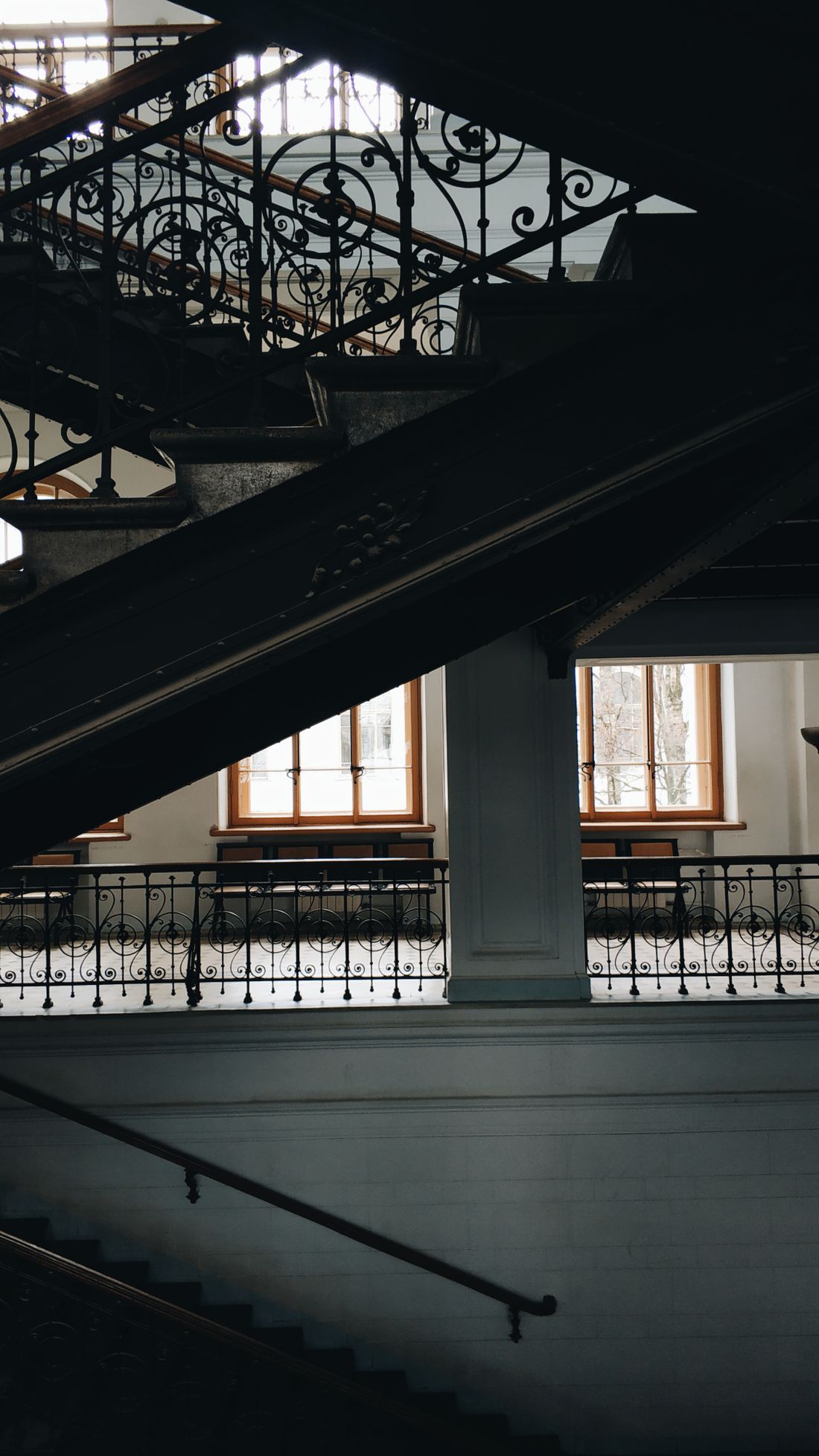 An empty ornate iron staircase inside a historic institutional building, with daylight coming through windows in the background