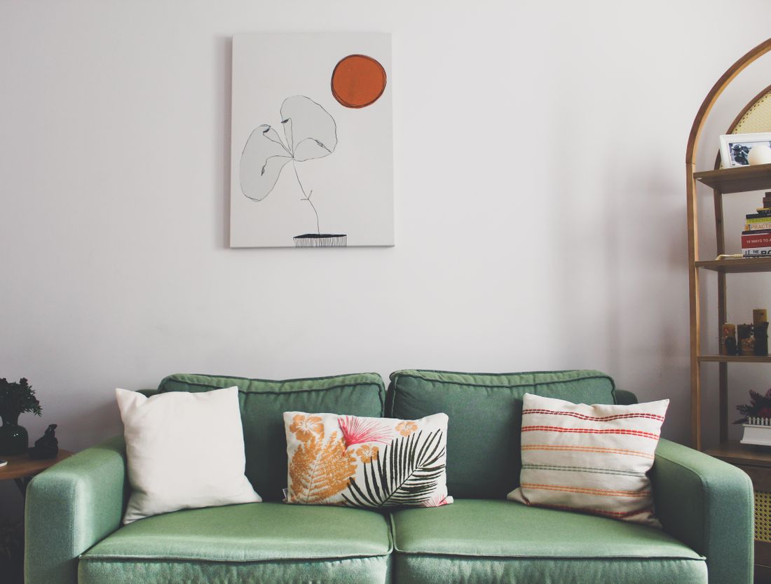 A furnished living room seen from across the room, with a single large canvas hanging on a plain wall above a green sofa, showing the piece's scale against the room and furniture below it.