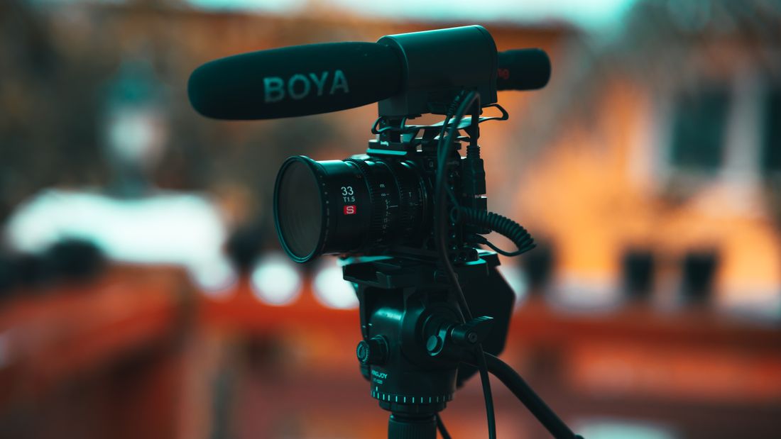 A directional shotgun microphone with a foam windscreen mounted on a video camera outdoors