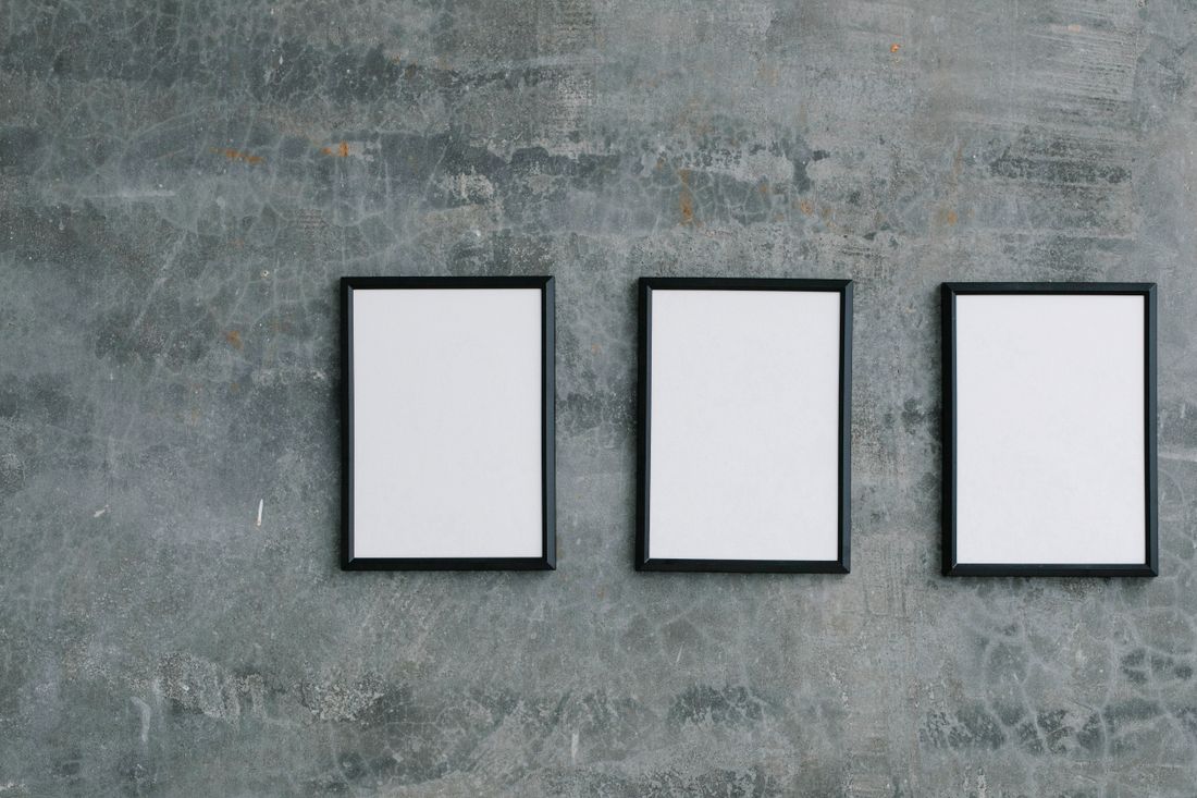 Three empty black picture frames of matching size mounted in a row on a textured gray concrete wall.
