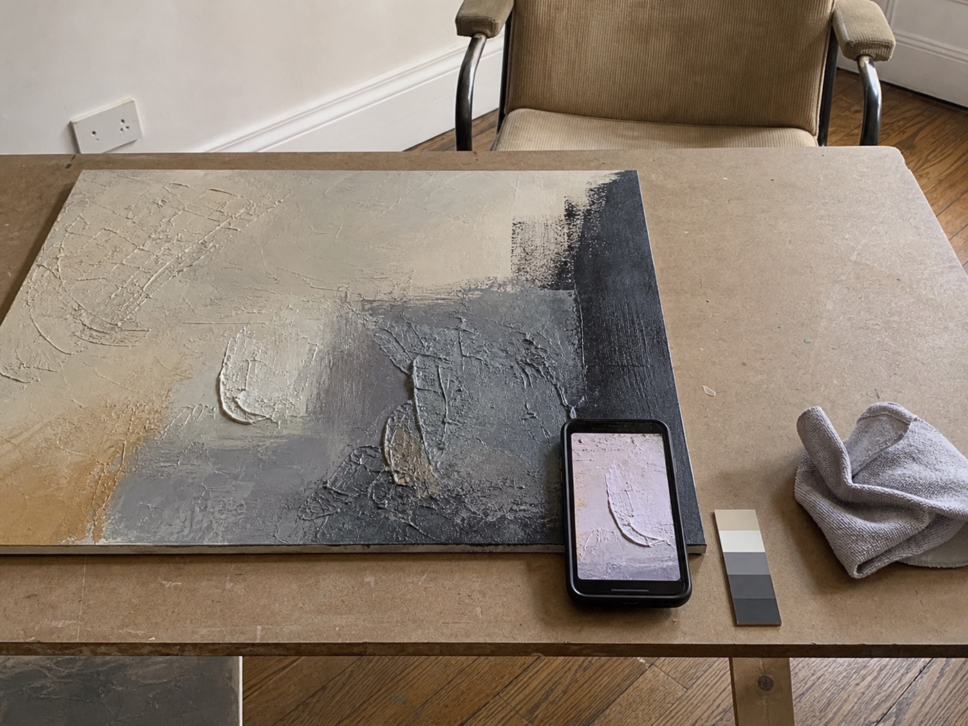 Phone-style behind-the-scenes view of a textured artwork detail beside a smartphone and color card