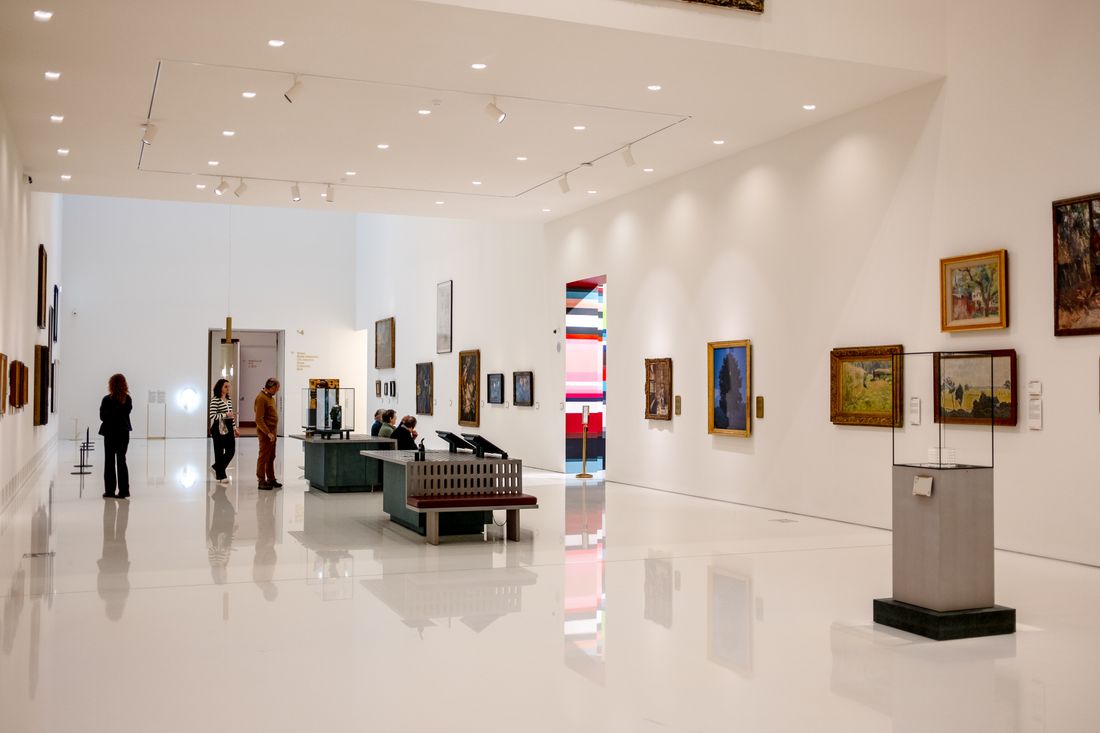 A bright white-walled gallery interior with framed works hung along both sides of a long room
