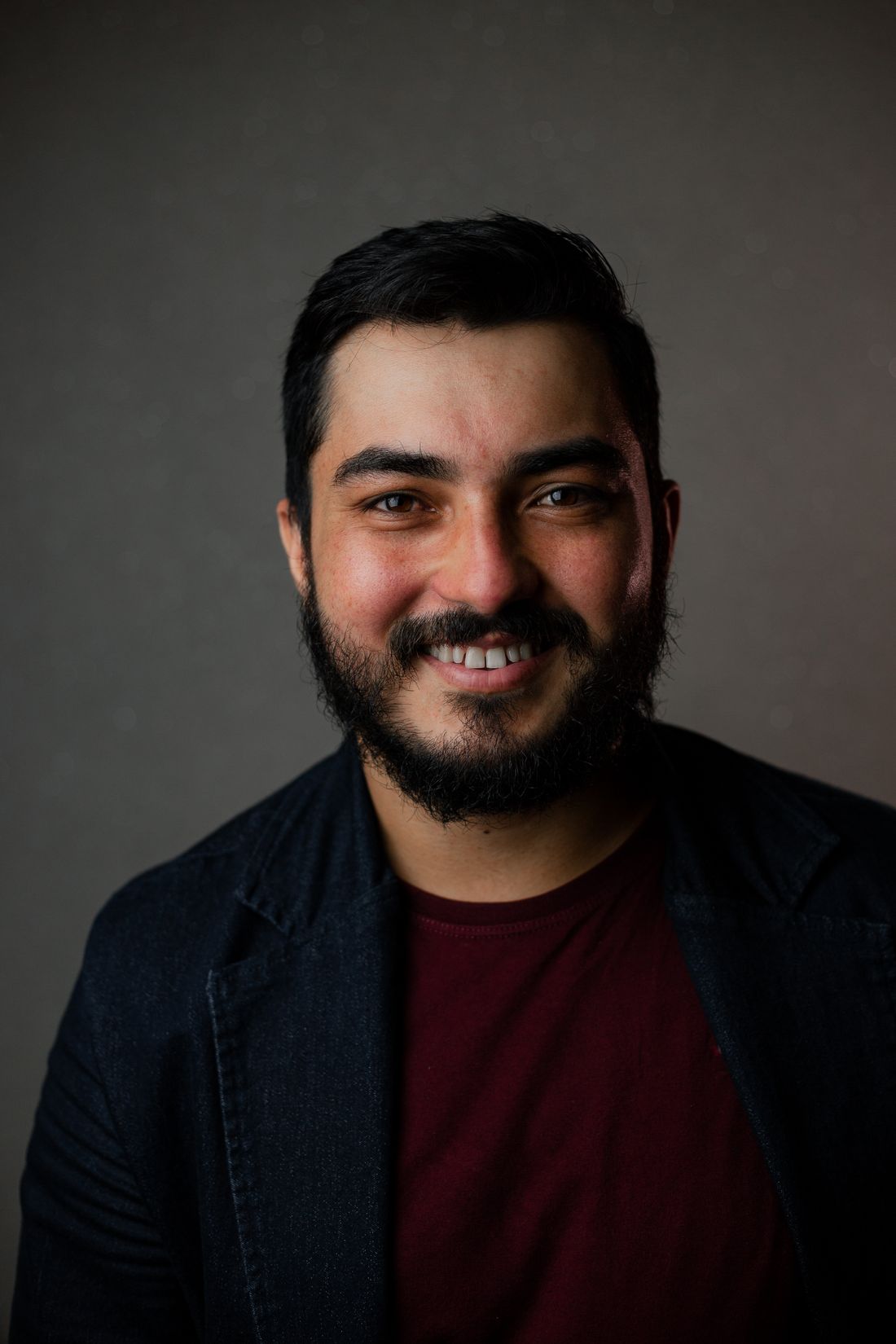 A close, natural portrait of a smiling man against a plain studio-style background