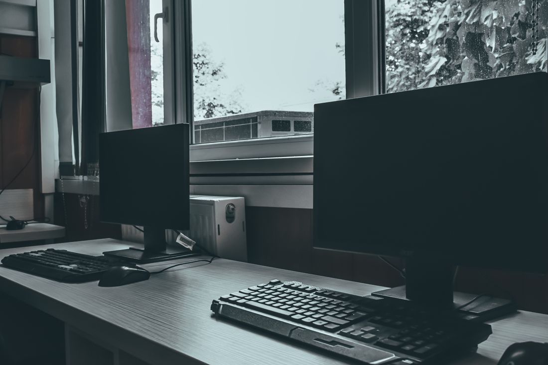 Two blank computer monitors on a desk near a window, screens off
