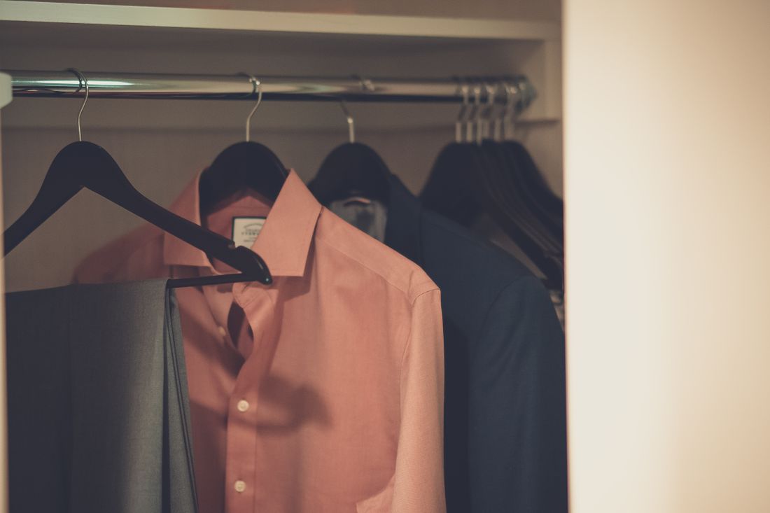 A tailored suit and a dress shirt hanging ready in a closet