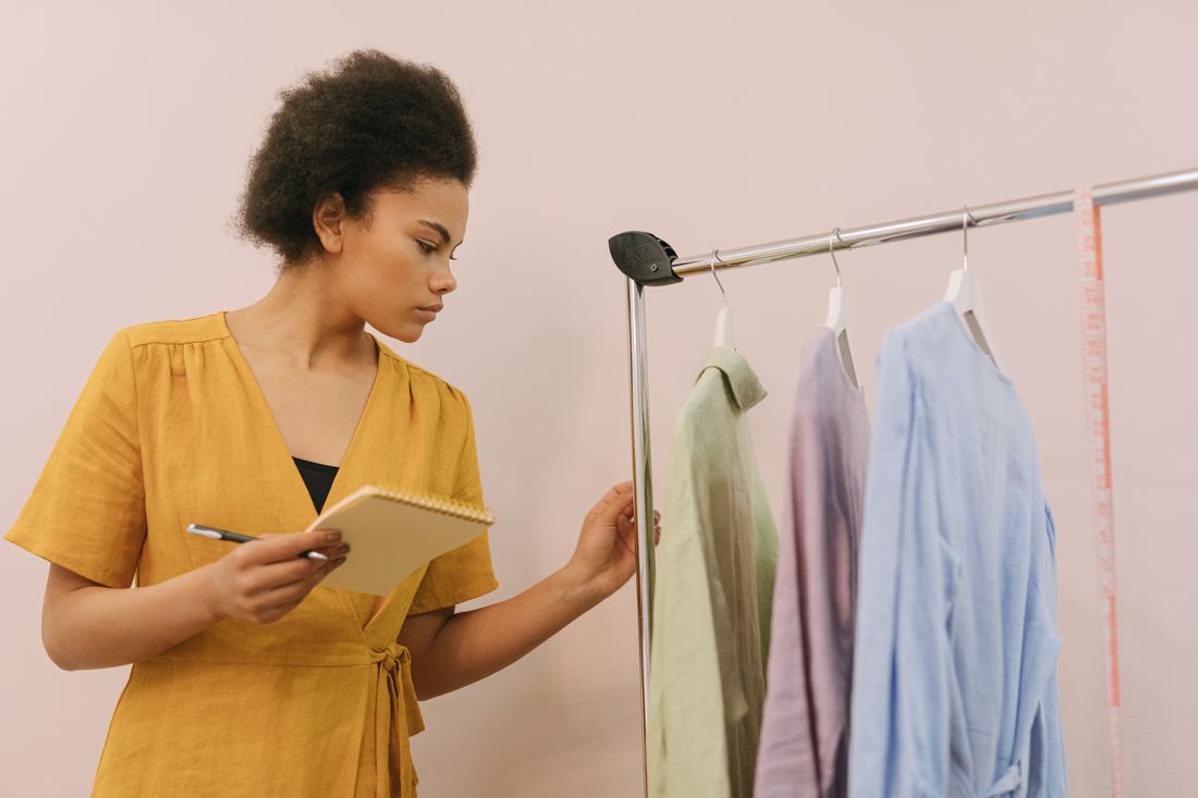 A stylist taking notes while reviewing a rack of color-coordinated garments in a studio