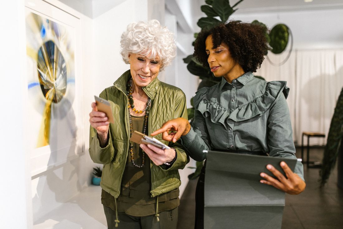 Two visitors looking closely at framed artwork on a gallery wall