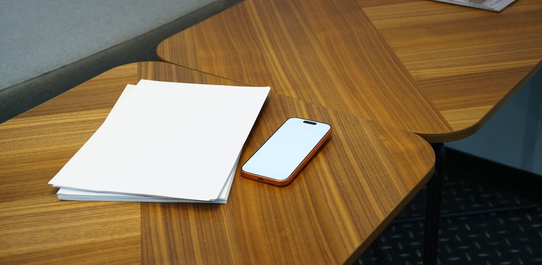 Minimalist desk setup with a stack of blank papers and a smartphone on a wooden table.