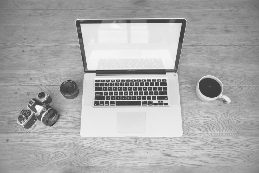 Camera, laptop, and coffee cup arranged casually on a wooden desk