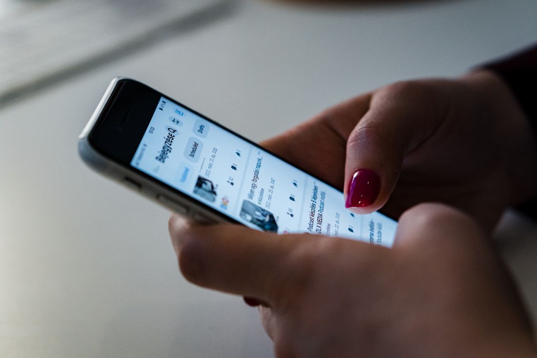 A close-up of a hand holding a smartphone and scrolling through a social media feed