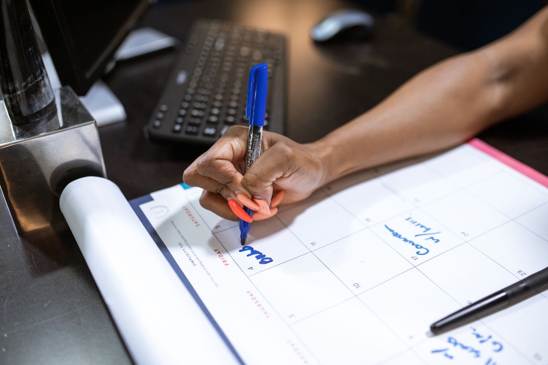A hand writing a note on a paper planning calendar with a blue marker