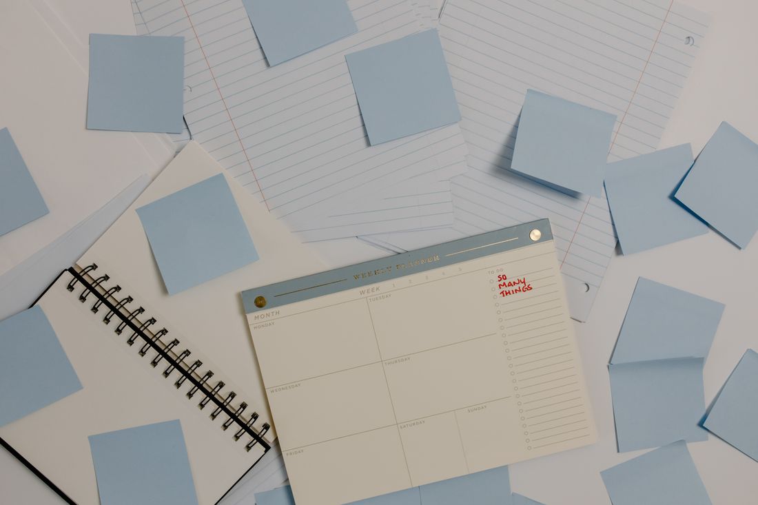 Overhead view of blank blue sticky notes and a day planner spread across a white desk