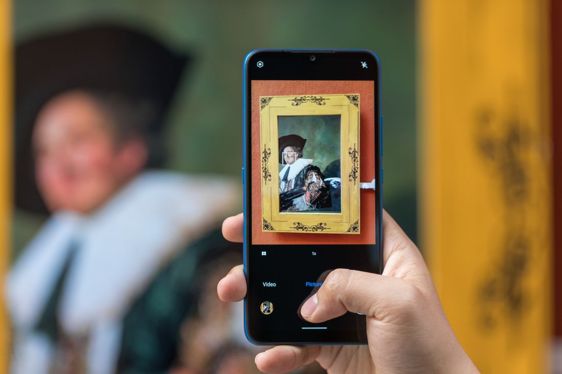 A hand holding a phone up to photograph a small framed painting for a social post