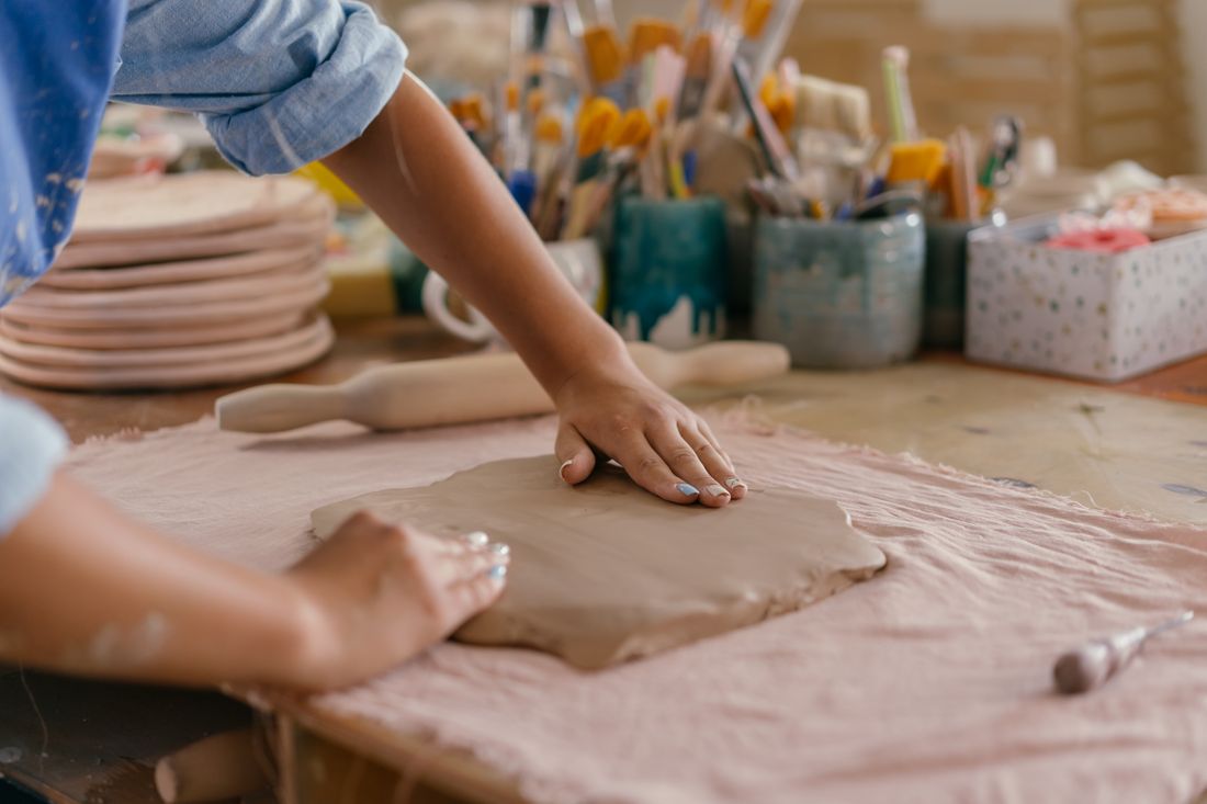 Close-up of hands shaping a sheet of clay on a work table in a pottery studio