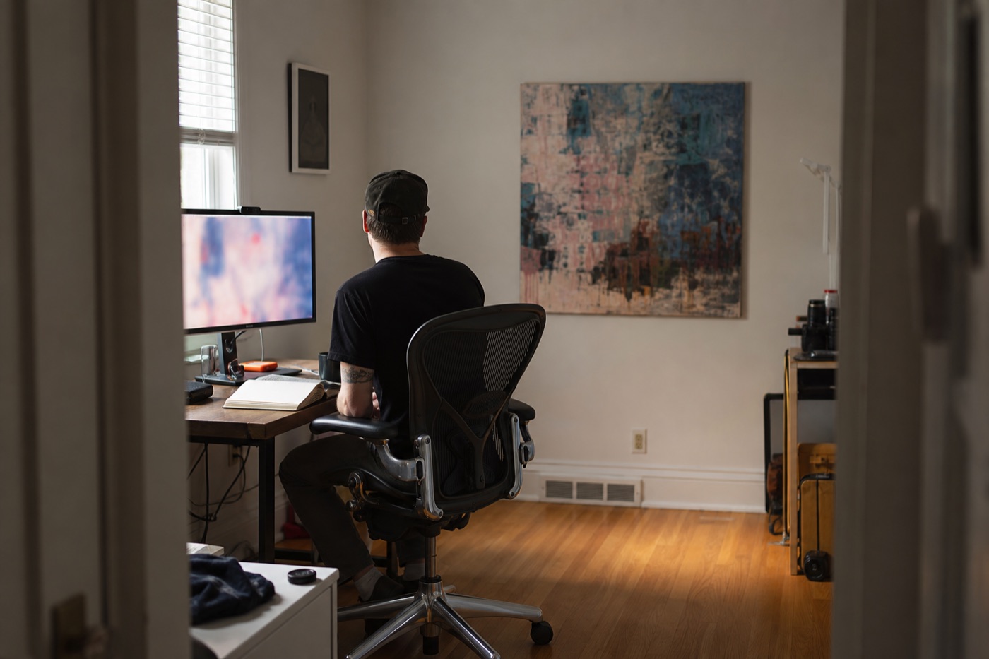 Editor comparing a blurred digital artwork image on a monitor with the physical painting hanging across the room