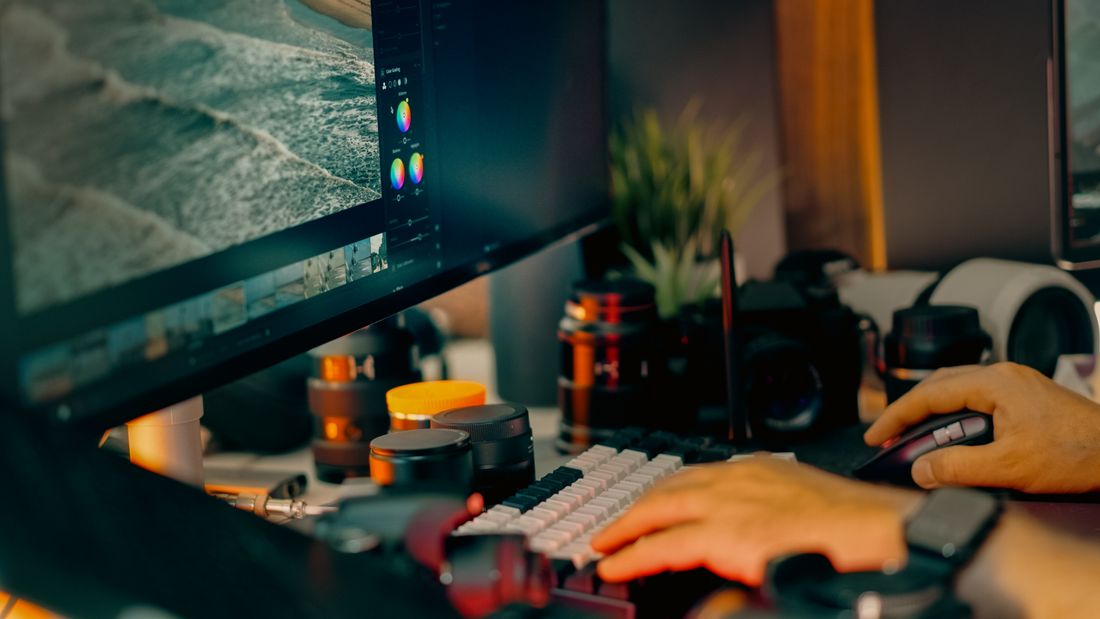 Digital editing workspace with a computer screen showing photo editing software, surrounded by camera equipment