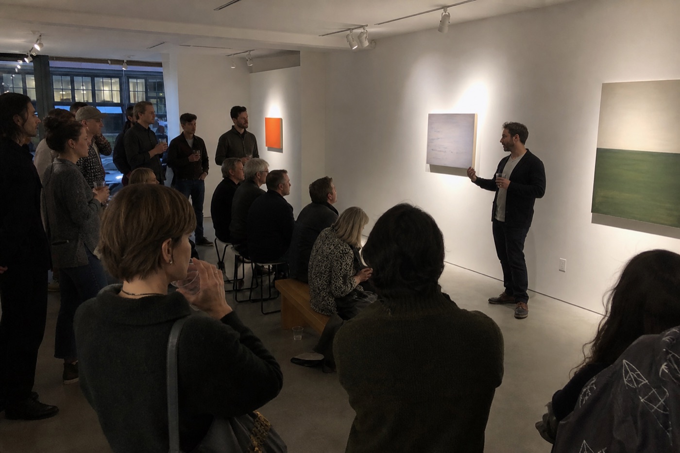 Artist speaking to a small audience inside a contemporary gallery opening
