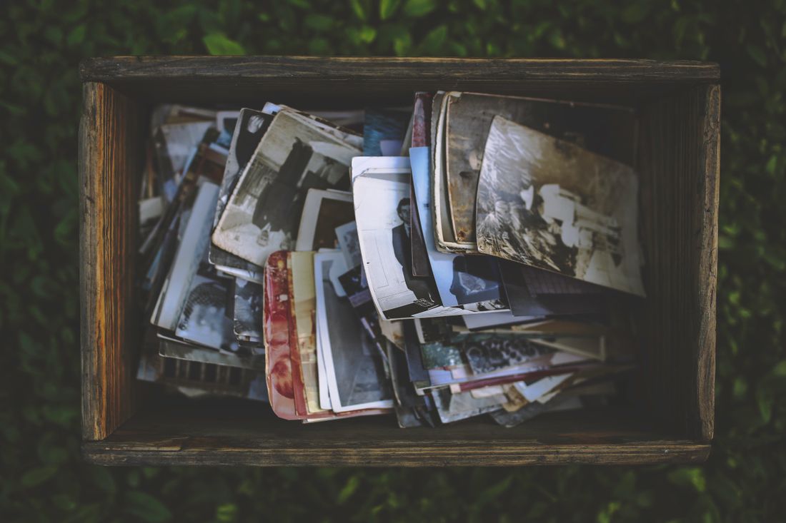 An open wooden box filled with a collection of old printed photographs
