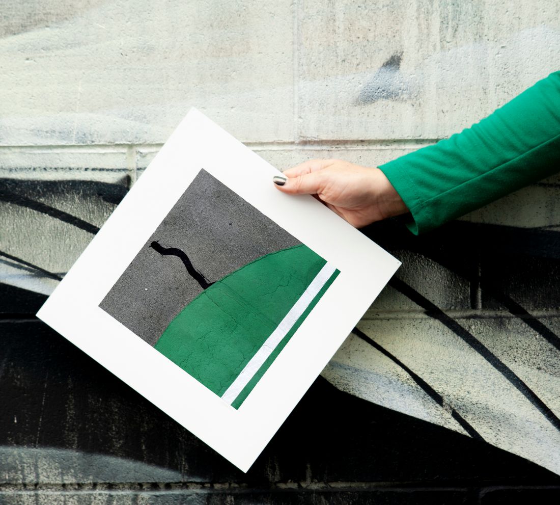 A hand holding a green and black abstract art print against a painted wall
