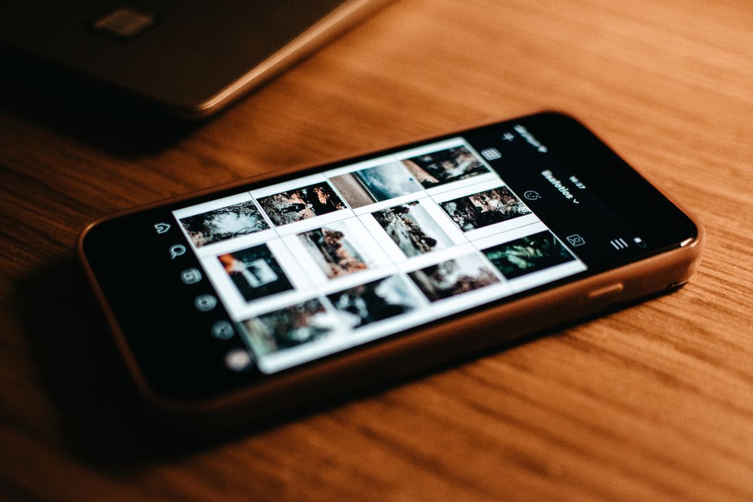 Close-up of a smartphone on a wooden desk showing a grid of photos ready to review