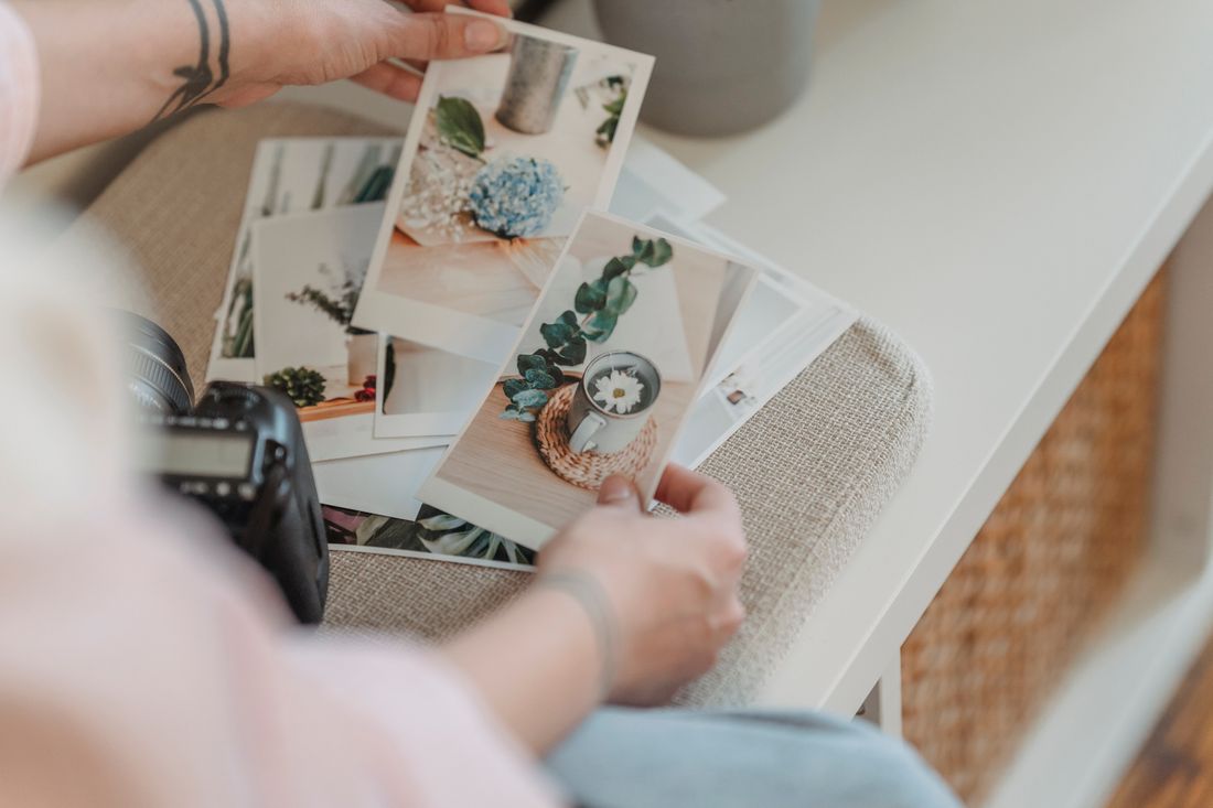A person looking down at printed photographs spread across a table, reviewing an archive of images