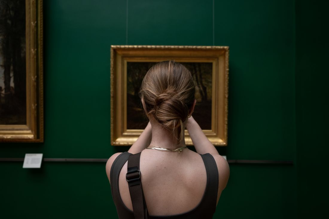 Back view of a photographer taking a picture of a painting on a gallery wall