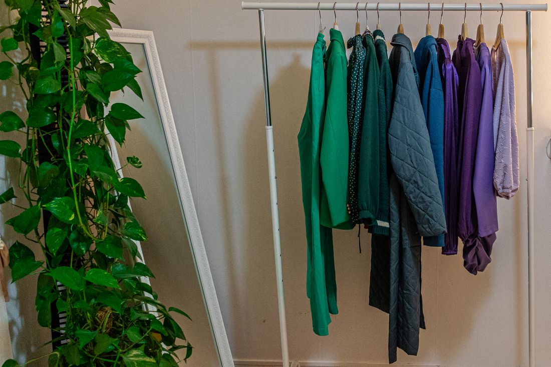 A clothes rack of colorful garments beside a mirror and a trailing ivy plant