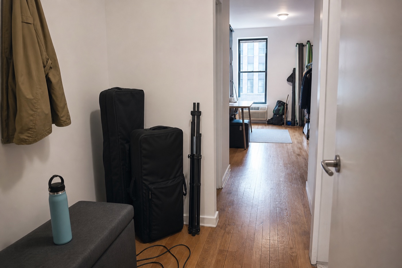 Narrow modern apartment hallway with compact black equipment cases, a folded stand, and a clear walking path