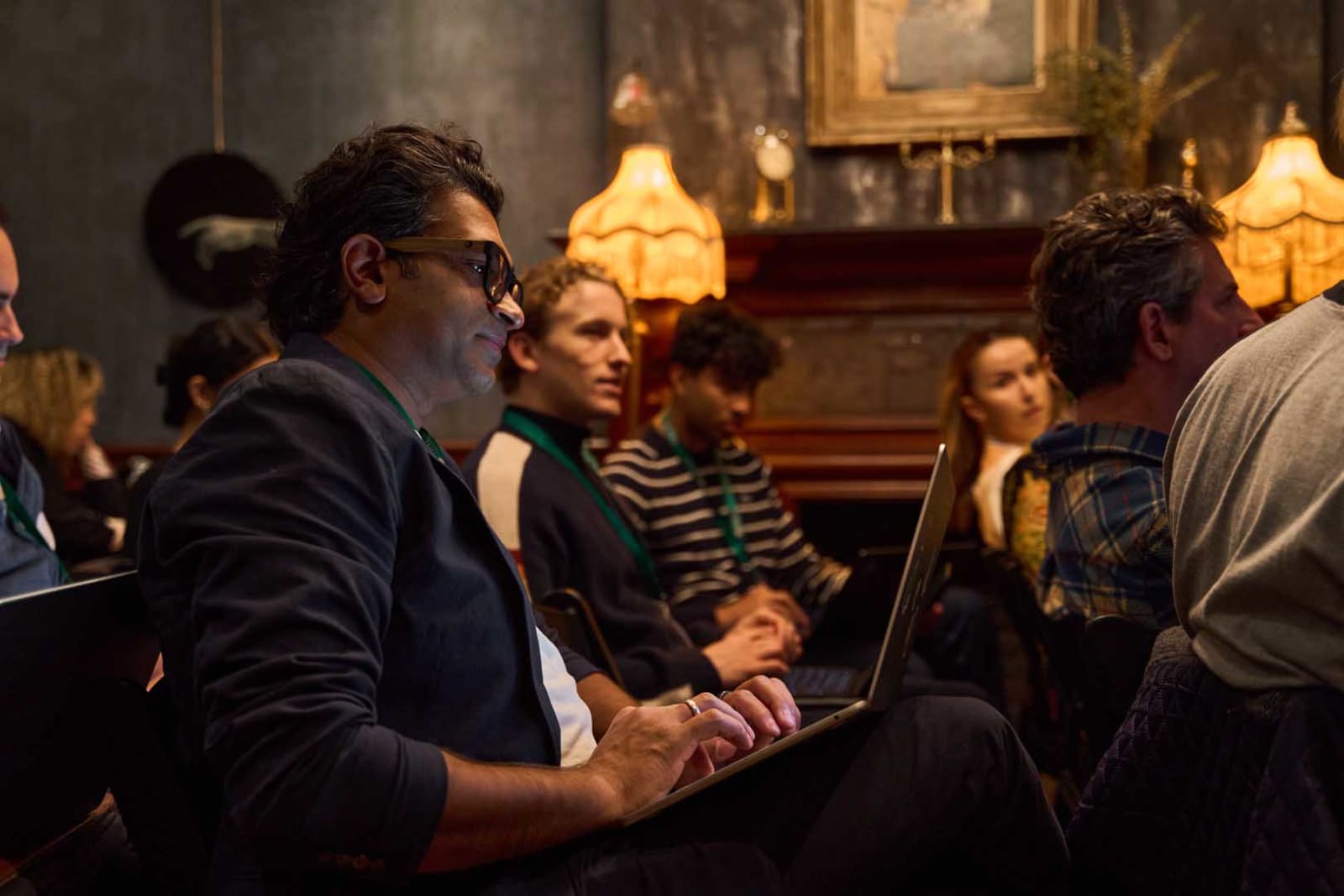 A packed room during an evening art event, guests seated close together