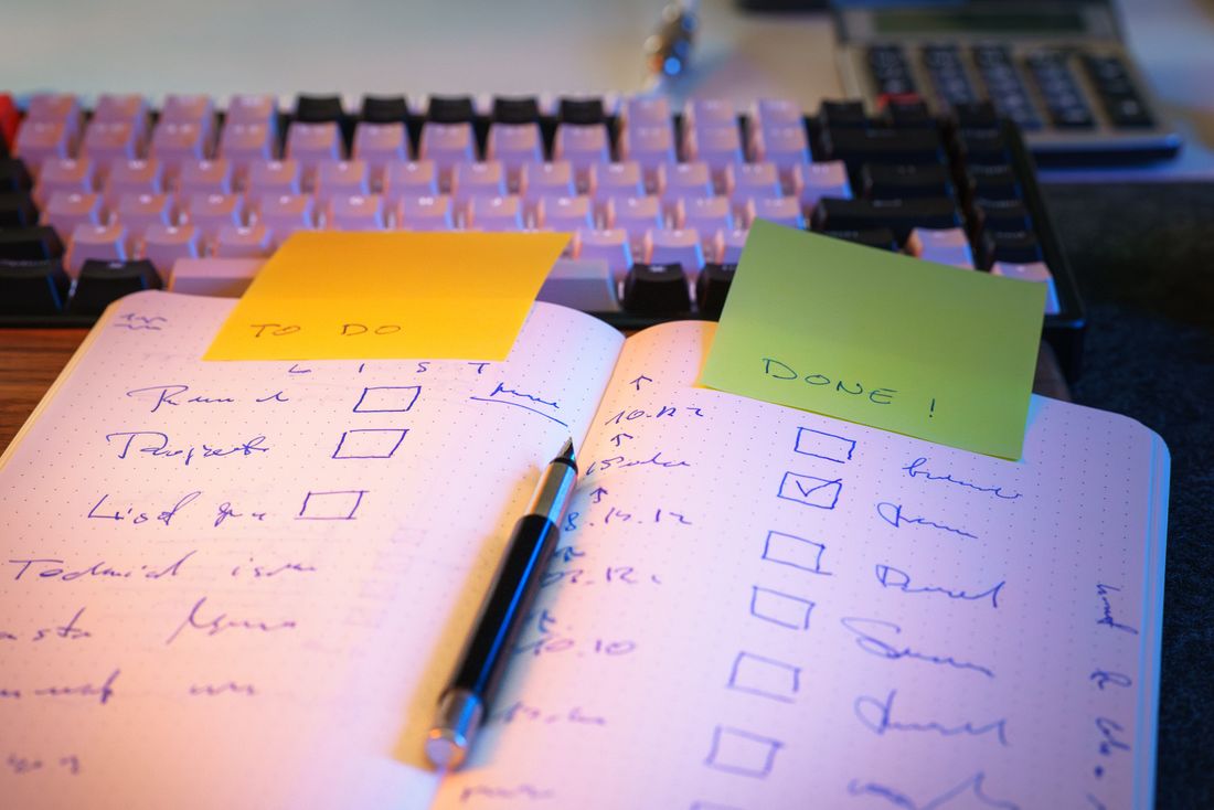 A handwritten to-do and done checklist in a notebook on a desk with a keyboard nearby