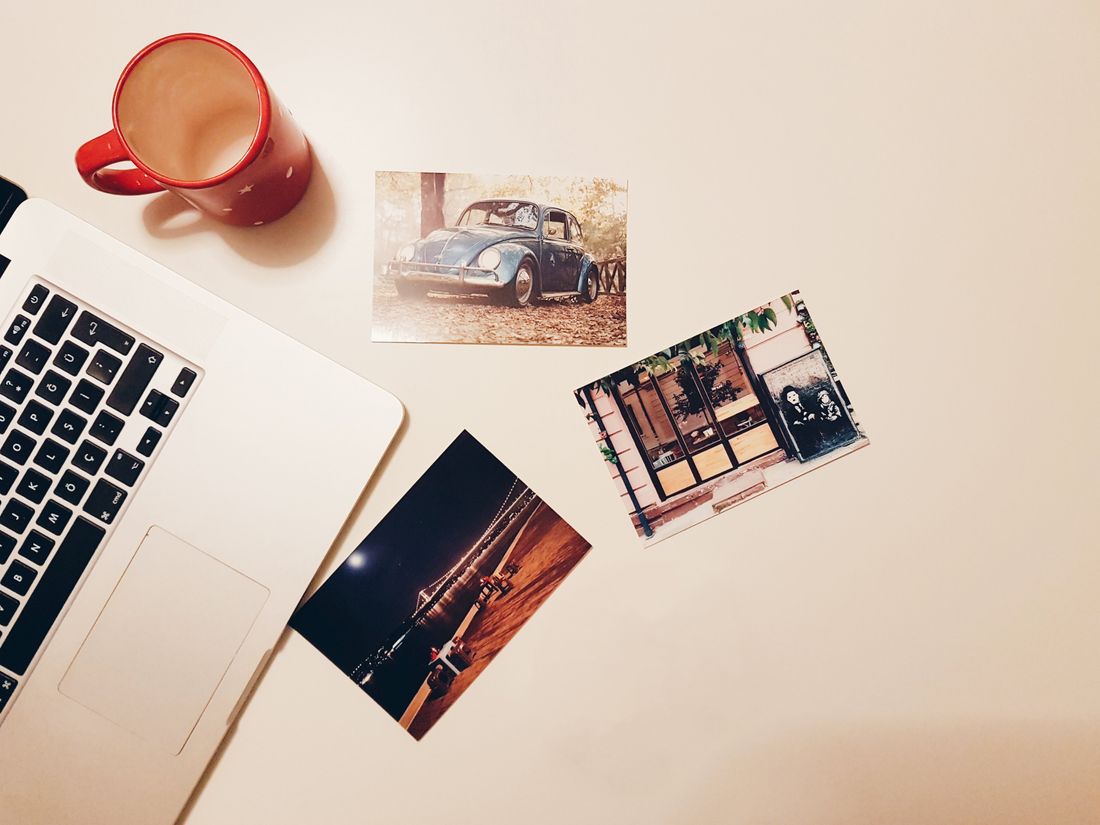 Printed photos next to an open laptop and a mug on a desk, as if being reviewed before updating a website
