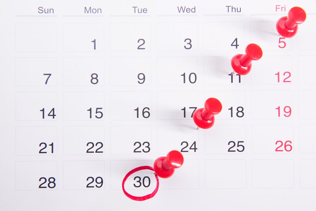 A wall calendar with several dates marked by red pins and one date circled