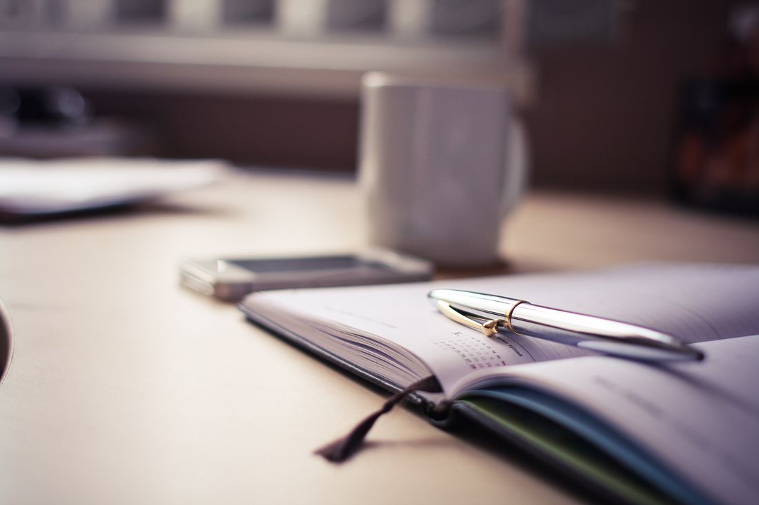 An open planner, a pen, and a coffee mug arranged on a wooden desk