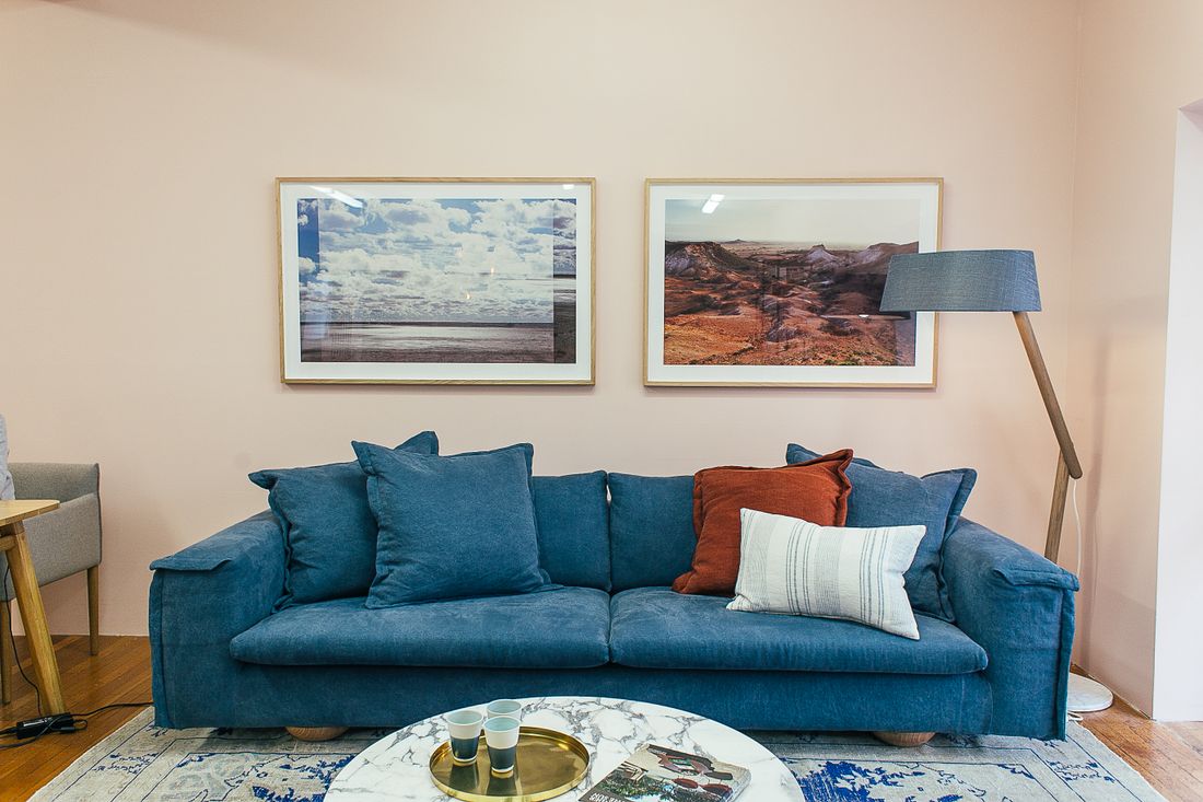 A domestic living room with a blue sofa and two large framed landscape photographs hung on the wall above it.