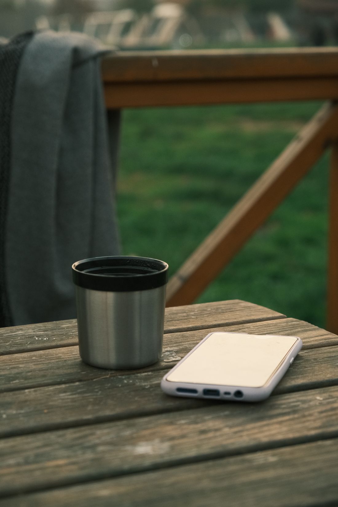 A phone resting screen-down next to a metal cup on a plain wooden table