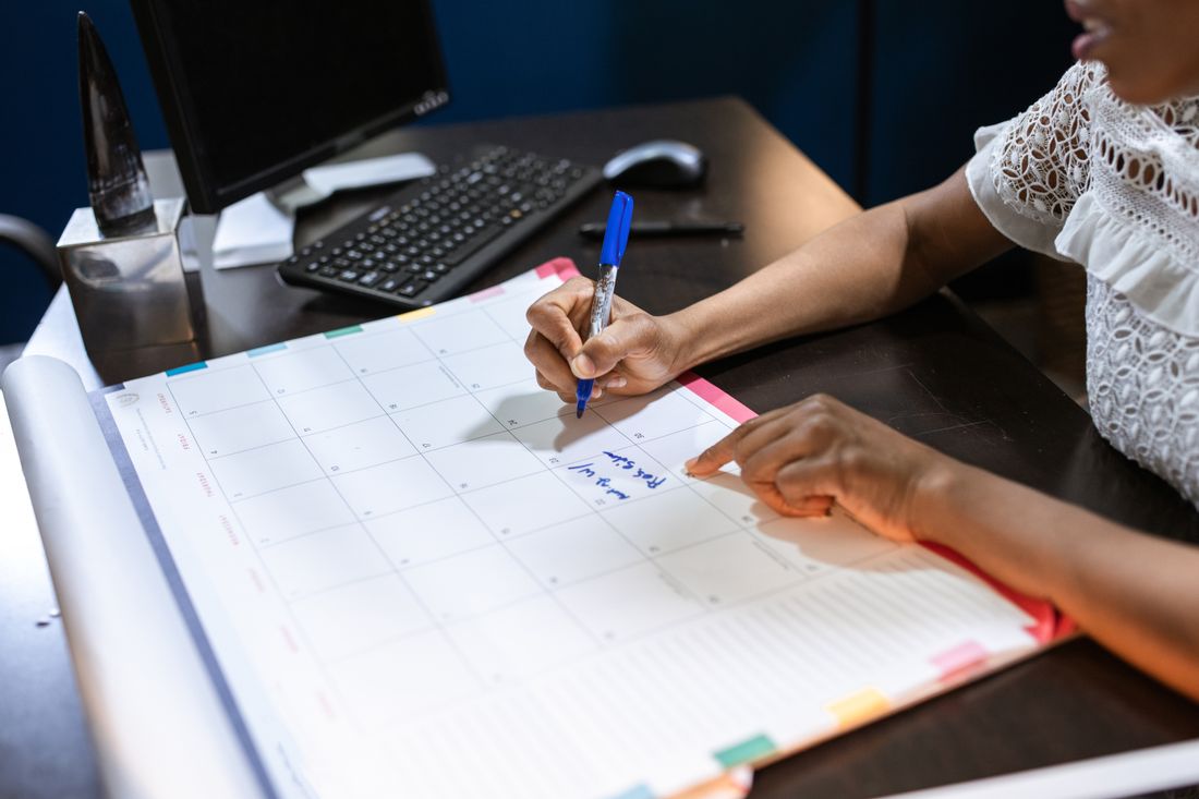 A hand marking a date on a large desk calendar with a pen
