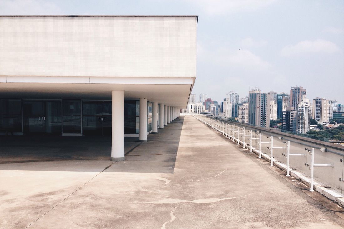 An empty, wide rooftop terrace with rows of white columns and a city skyline in the background