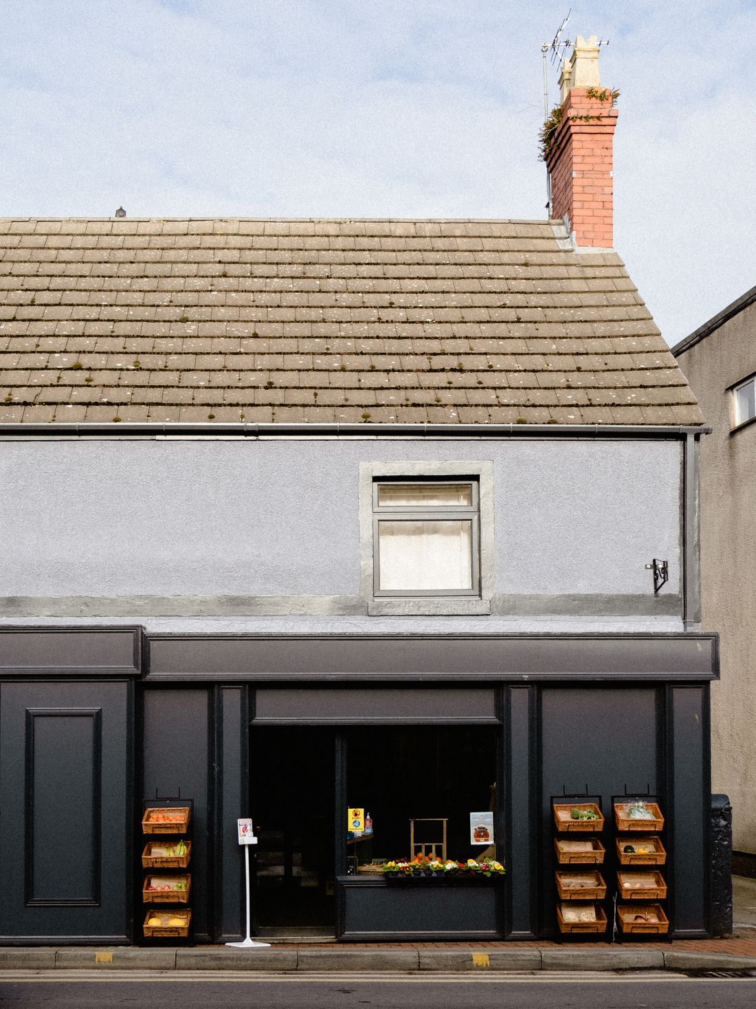 A small grocer's storefront with crates of produce displayed in baskets on either side of the entrance