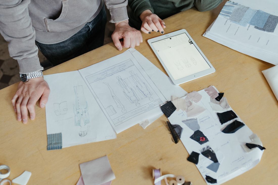 Two people reviewing clothing sketches and fabric swatches spread across a worktable