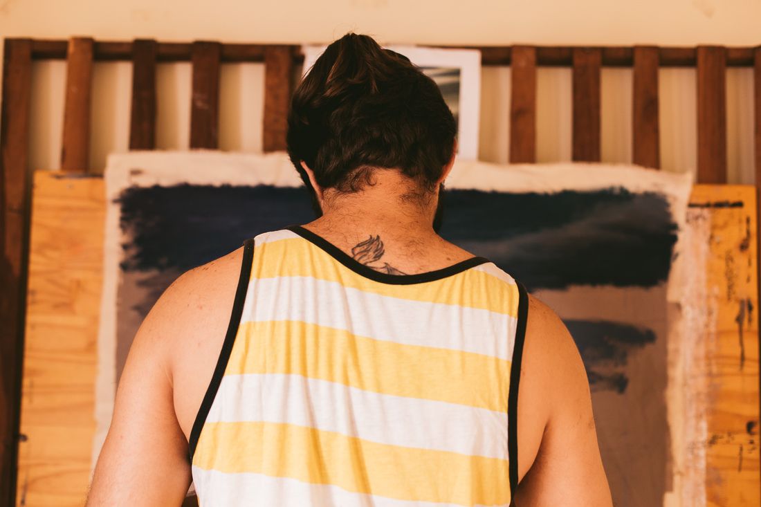 A person seen from behind in a striped cotton tank top, standing in front of a large partly painted canvas.