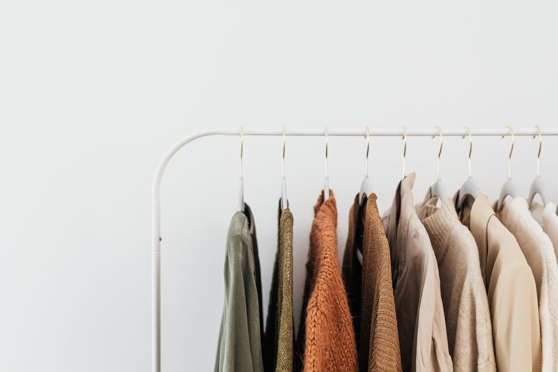 A dense rack of garments in muted earth tones hanging on a plain white wall, no people in frame