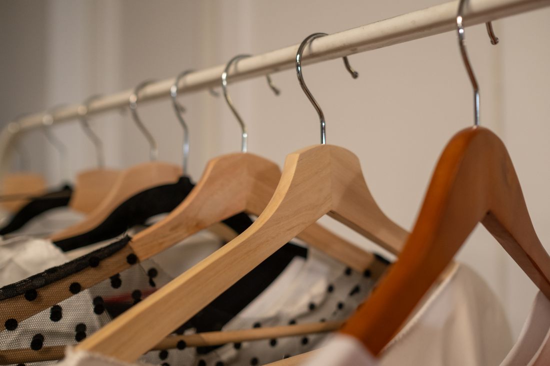 A close view of wooden hangers along a clothing rail, shallow depth of field, neutral tones, no hands or faces in frame