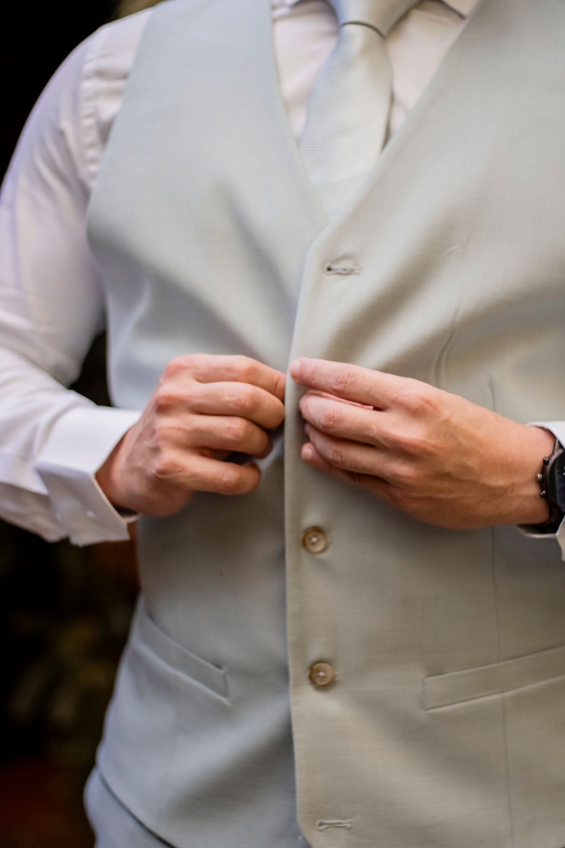 Close-up vertical view of a pair of hands buttoning a plain vest, no face visible