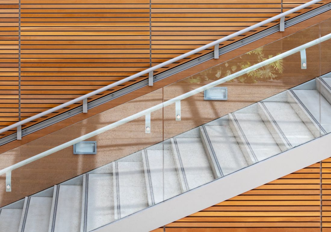 A plain modern staircase seen from above, with a glass railing and a wood-slat wall, no one on the stairs.