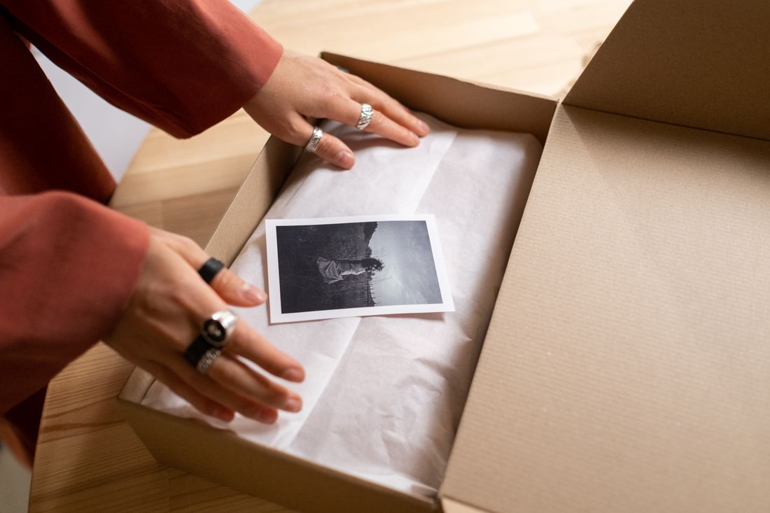 Hands carefully unwrapping a single printed photograph from archival tissue paper inside a box.