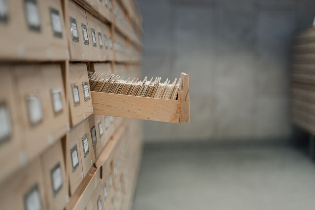An open archive drawer holding rows of stored index cards, part of a larger wall of storage drawers.