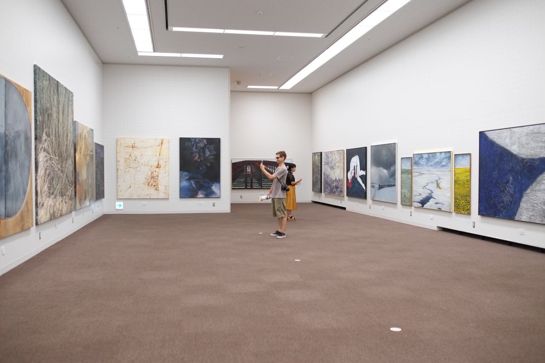 Visitors walking through a bright gallery filled with paintings.